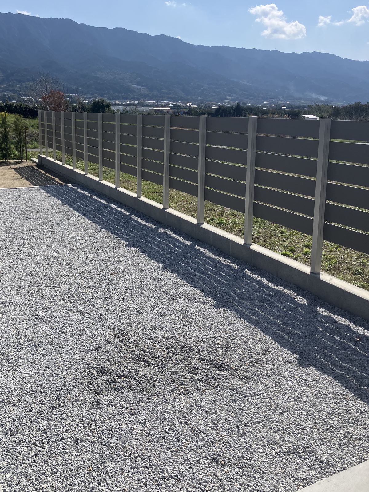 山並みを背景に連なるプラド/oneの人工木フェンス（福岡県久留米市田主丸町の施工実績）